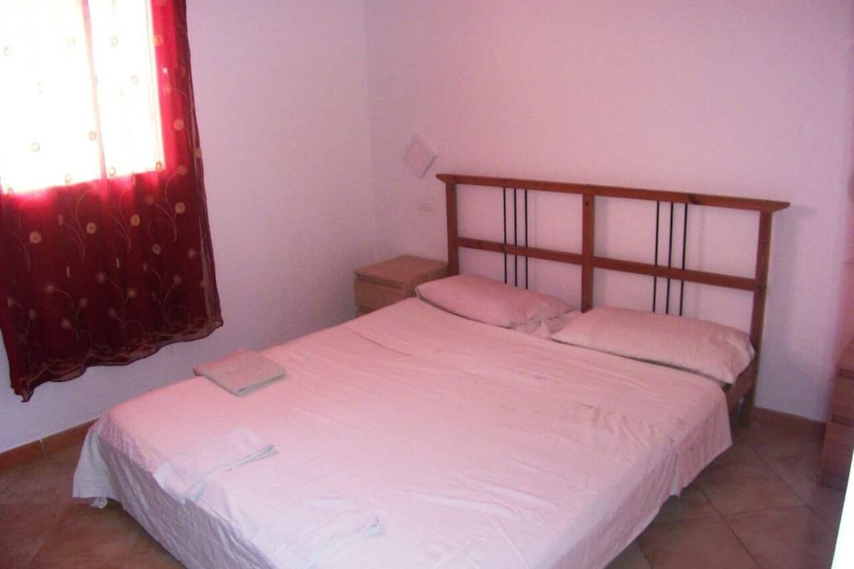 A single bed with a wooden headboard, a bedside table, and a window with curtains.