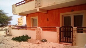 A two-story building with a stone entrance, a gated driveway, and a small garden with plants. - costa do sol (Boa Vista)