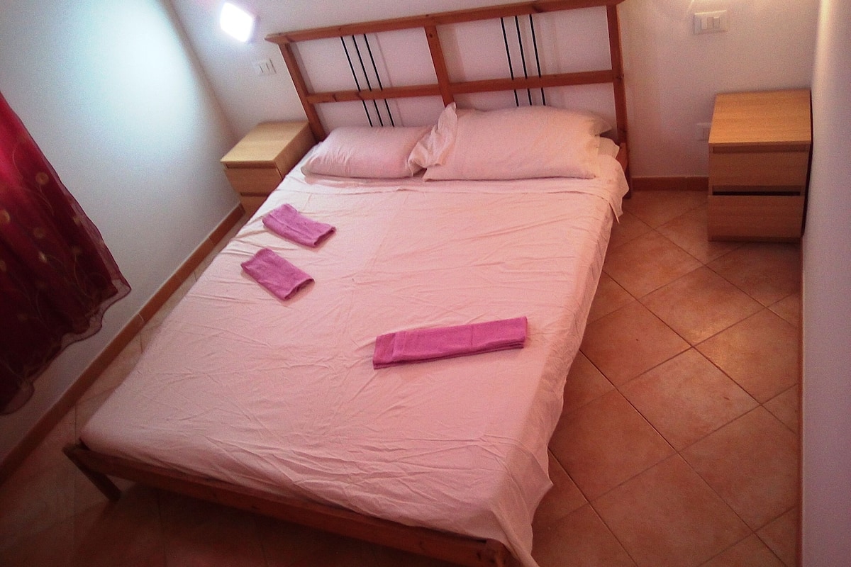 A single bed with a wooden frame, two pillows, and a pink bedspread. There are two wooden nightstands with drawers, one on each side of the bed.