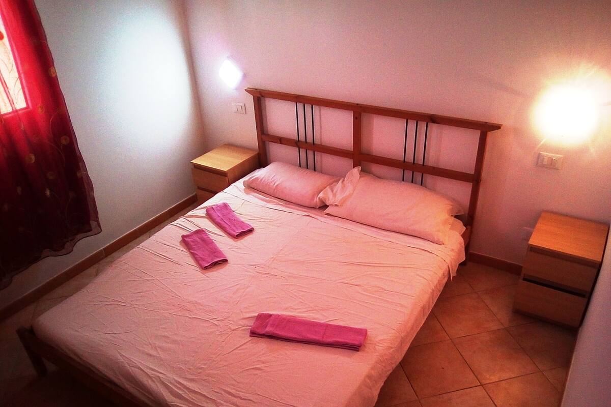 A single bed with a wooden headboard, two bedside tables, and a wall-mounted light.