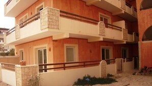 A multi-story residential building with balconies, a stone base, and a sandy ground. - costa do sol (Boa Vista)
