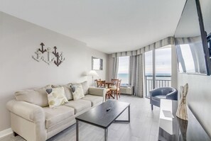 Ett modernt vardagsrum med en soffa, ett soffbord och en matplats. Det finns en balkong med utsikt över havet.