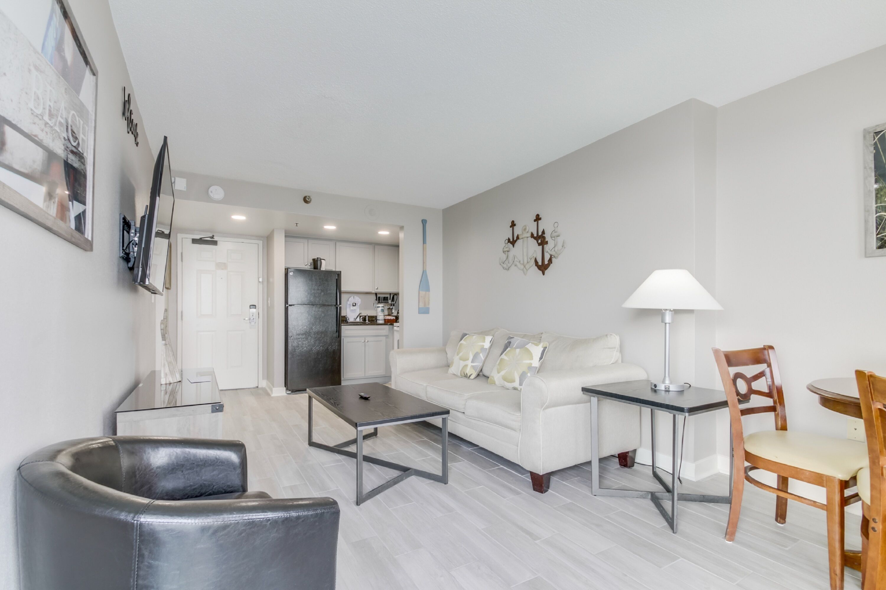 A modern living room with a sofa, coffee table, and chairs. There is a dining table with chairs. The room has a kitchen in the background.