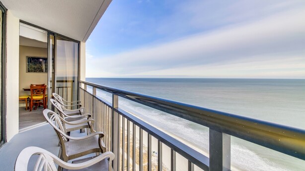 A balcony with a view of the ocean, a dining area with chairs, and a table. - Ocean Front Condos at Patricia Grand (Myrtle Beach)