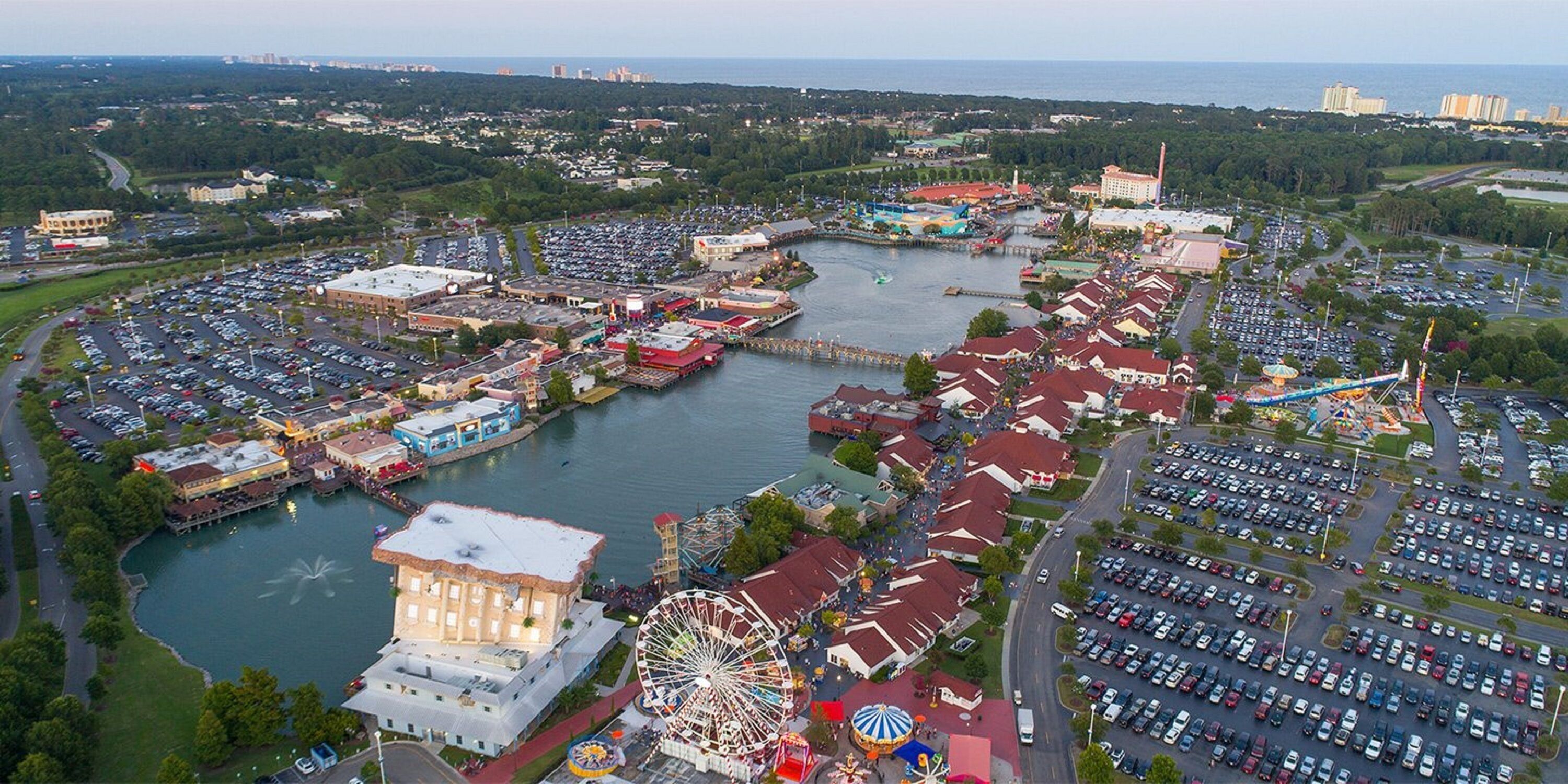 An aerial view of a waterfront amusement park with a Ferris wheel, a carousel, and a large body of water.