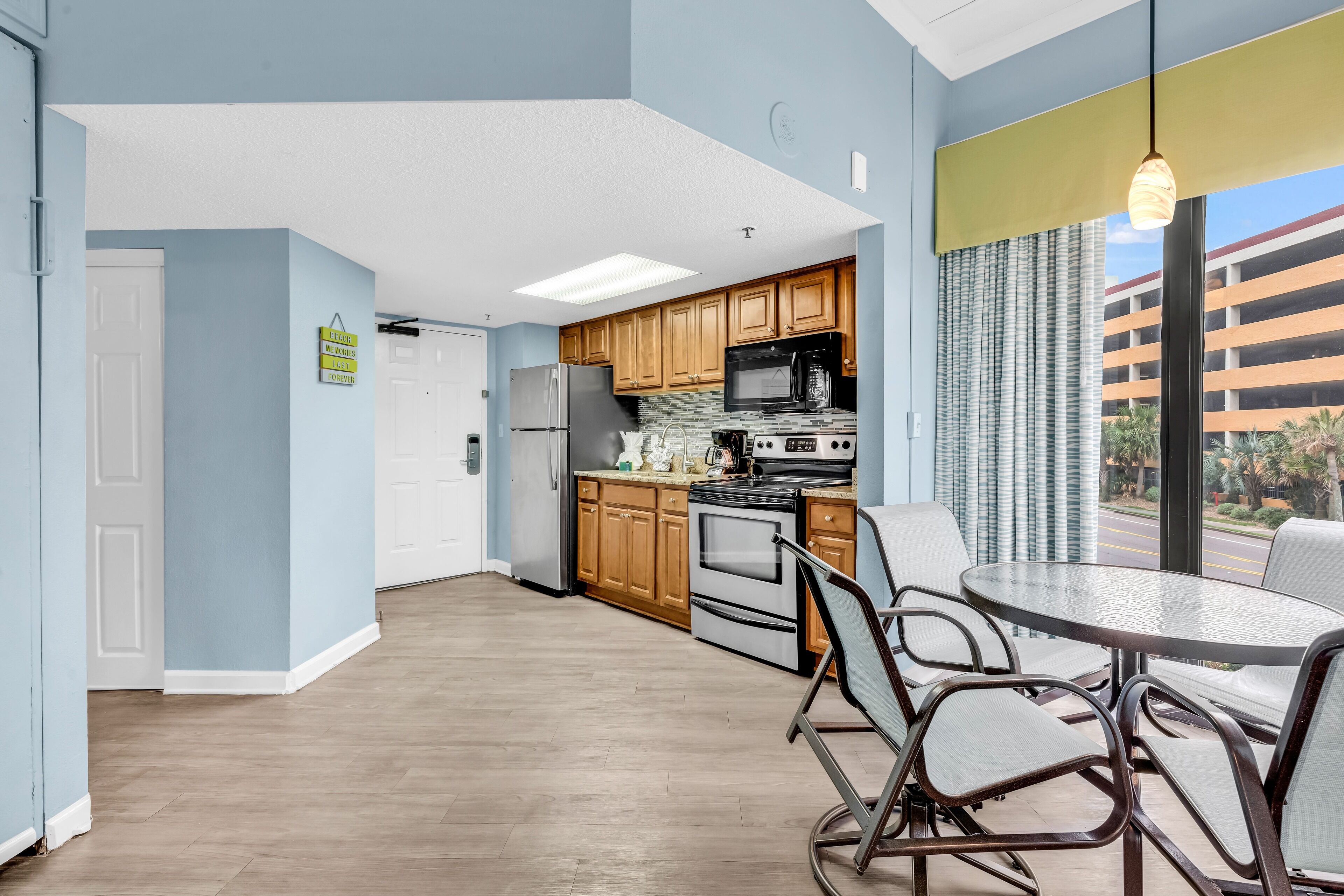 A modern kitchen with wooden cabinets, a stainless steel refrigerator, and a large window with a view of a building.