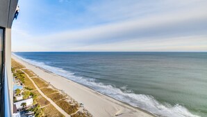 A coastal view from a high vantage point, featuring a beach, ocean, and a residential area with houses and a road. - Ocean Front Condos at Patricia Grand (Myrtle Beach)