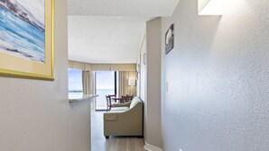 A hallway with a beige sofa, a dining table with chairs, and a painting on the wall. - Ocean Front Condos at Patricia Grand (Myrtle Beach)