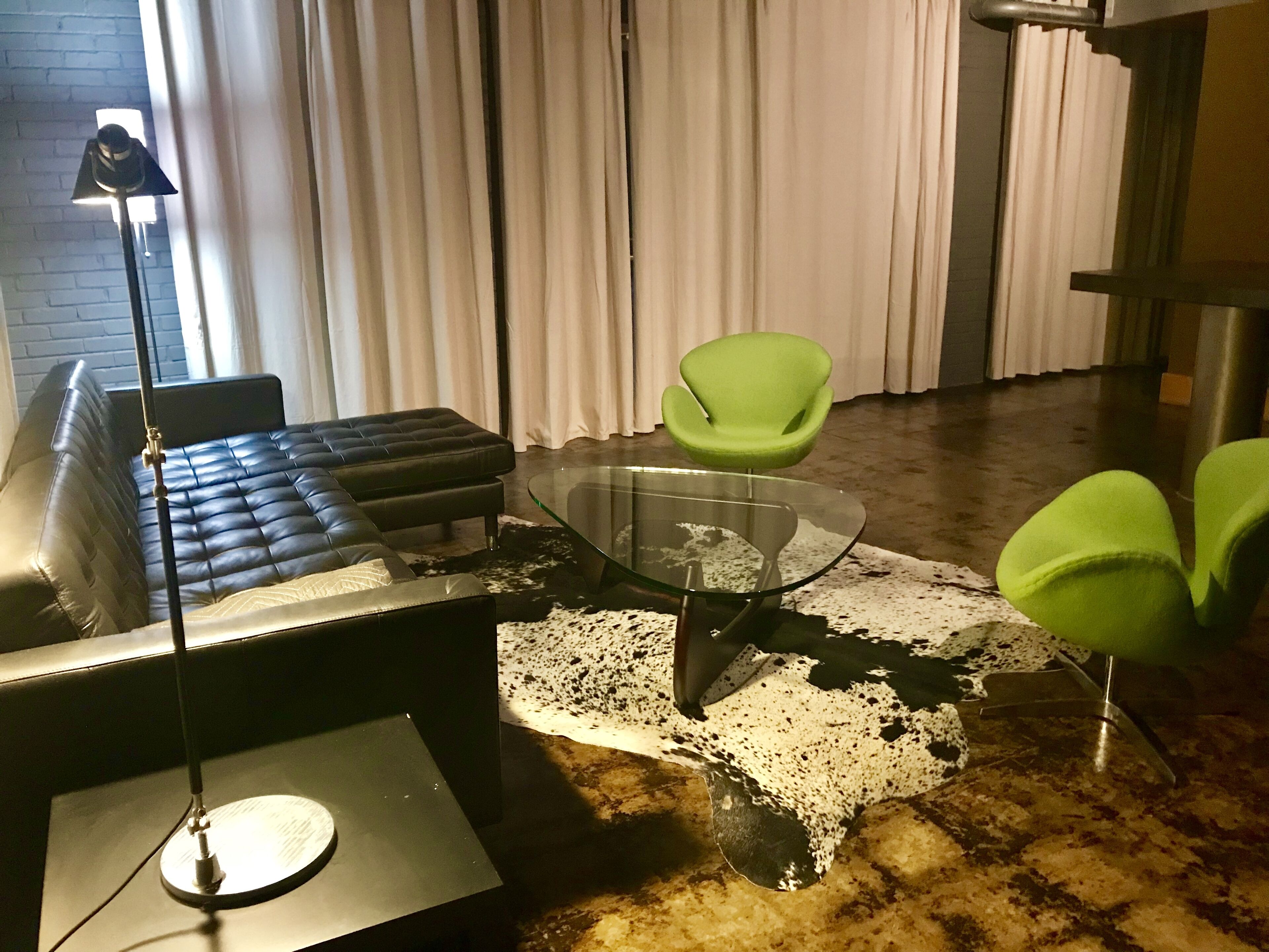 A modern living room with a glass coffee table, leather sofa, and green chairs.