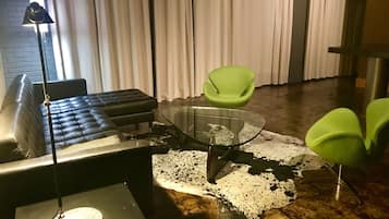 A modern living room with a glass coffee table, leather sofa, and green chairs.