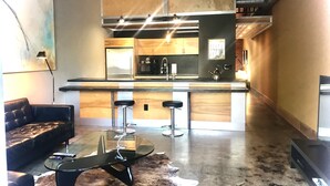 A modern kitchen with a central island, bar stools, and a dining area with a glass table. - The Hangar Lofts Hotel (Columbia)