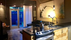 A modern kitchen with a built-in oven, a coffee maker, and a sink. There is a sliding glass door leading to a balcony with a blue chair and a table. - The Hangar Lofts Hotel (Columbia)