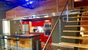 A modern kitchen with red cabinets, stainless steel appliances, and a bar area with stools. - The Hangar Lofts Hotel (Columbia)