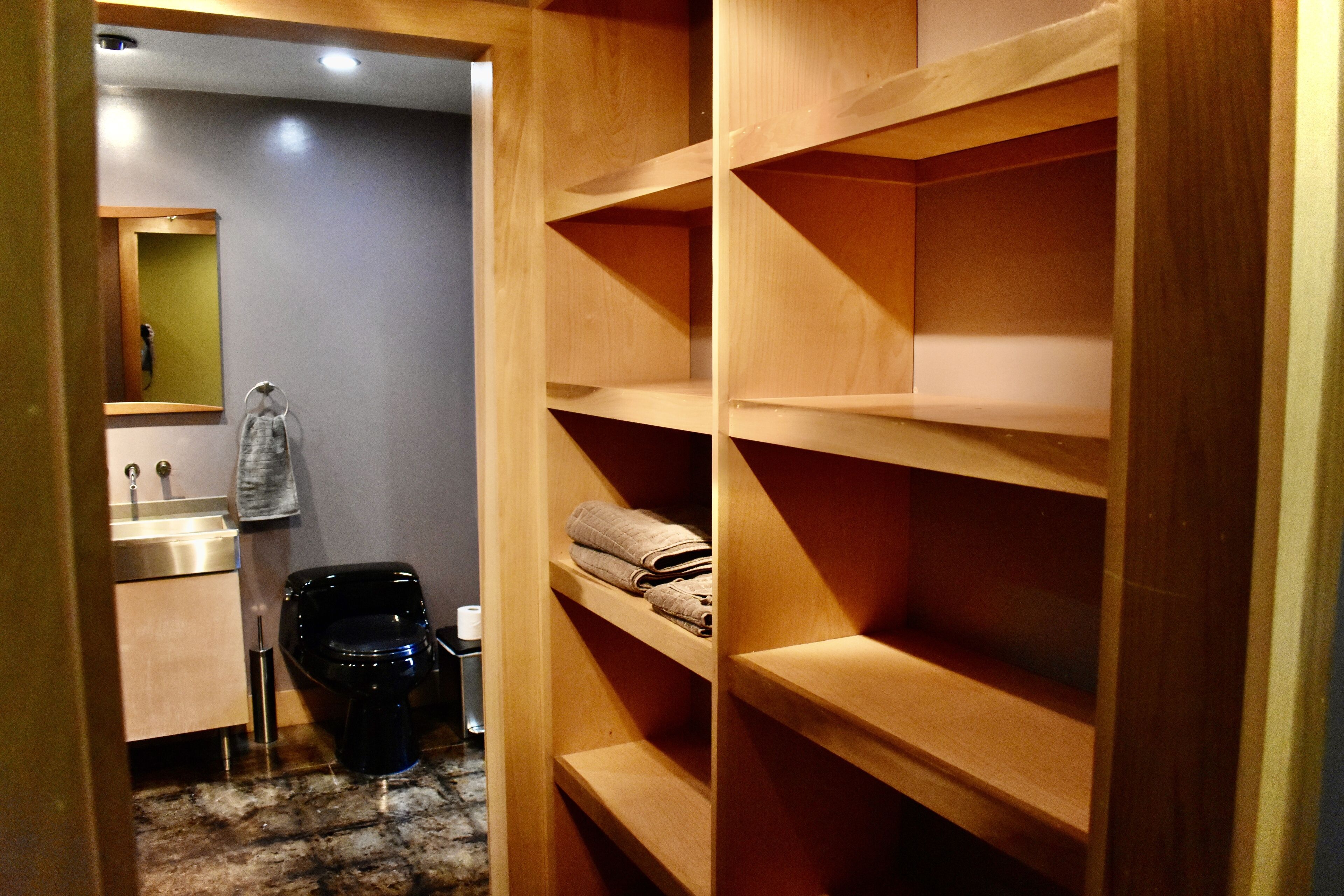 A bathroom with a wooden vanity, a toilet, and a shelf with folded towels.