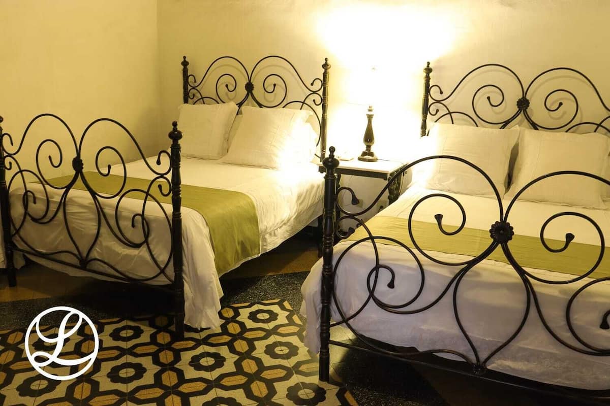 Two single beds with ornate metal frames, a patterned floor, and a nightstand with a lamp between them.