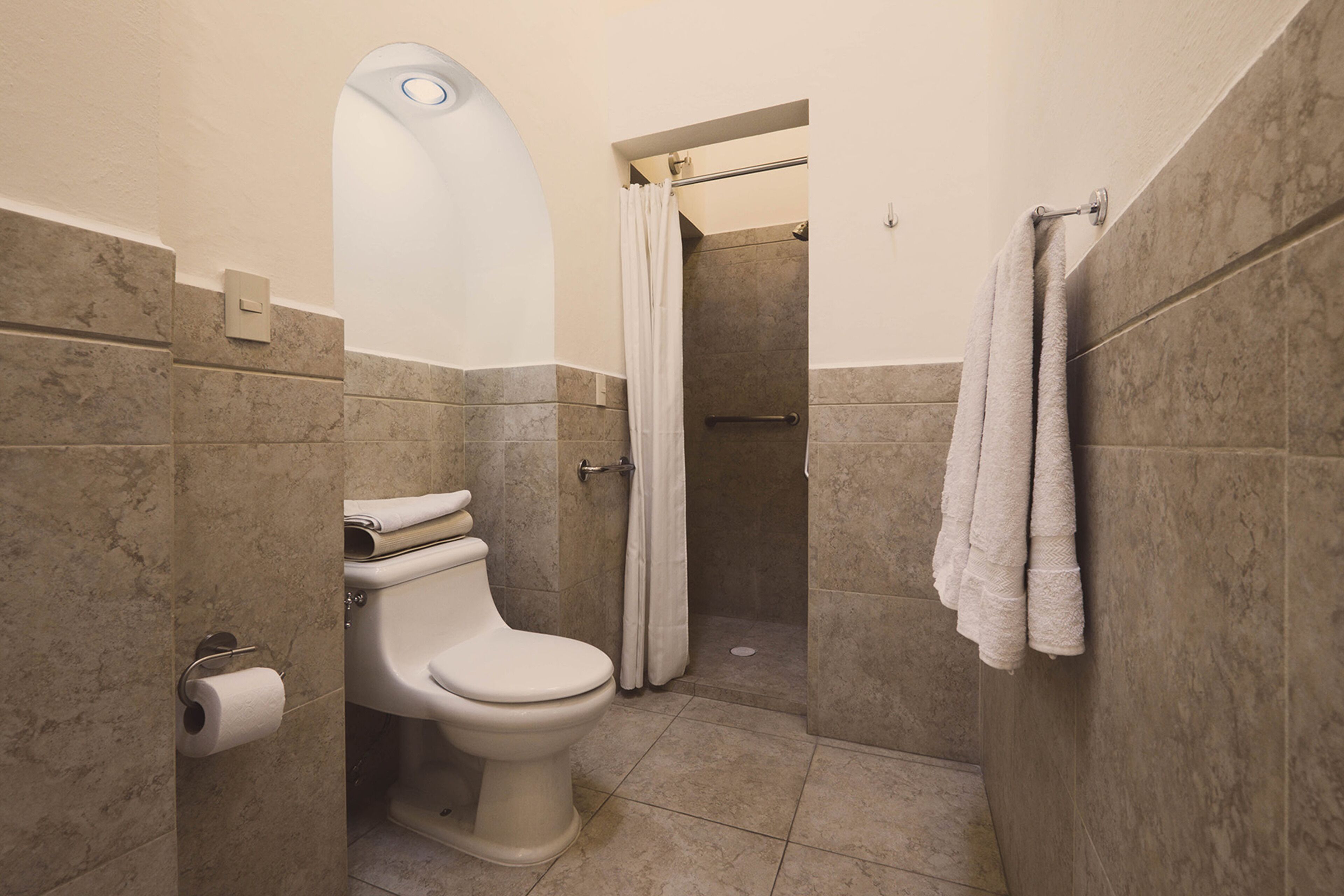 Un baño con inodoro, ducha y perchero para toallas.