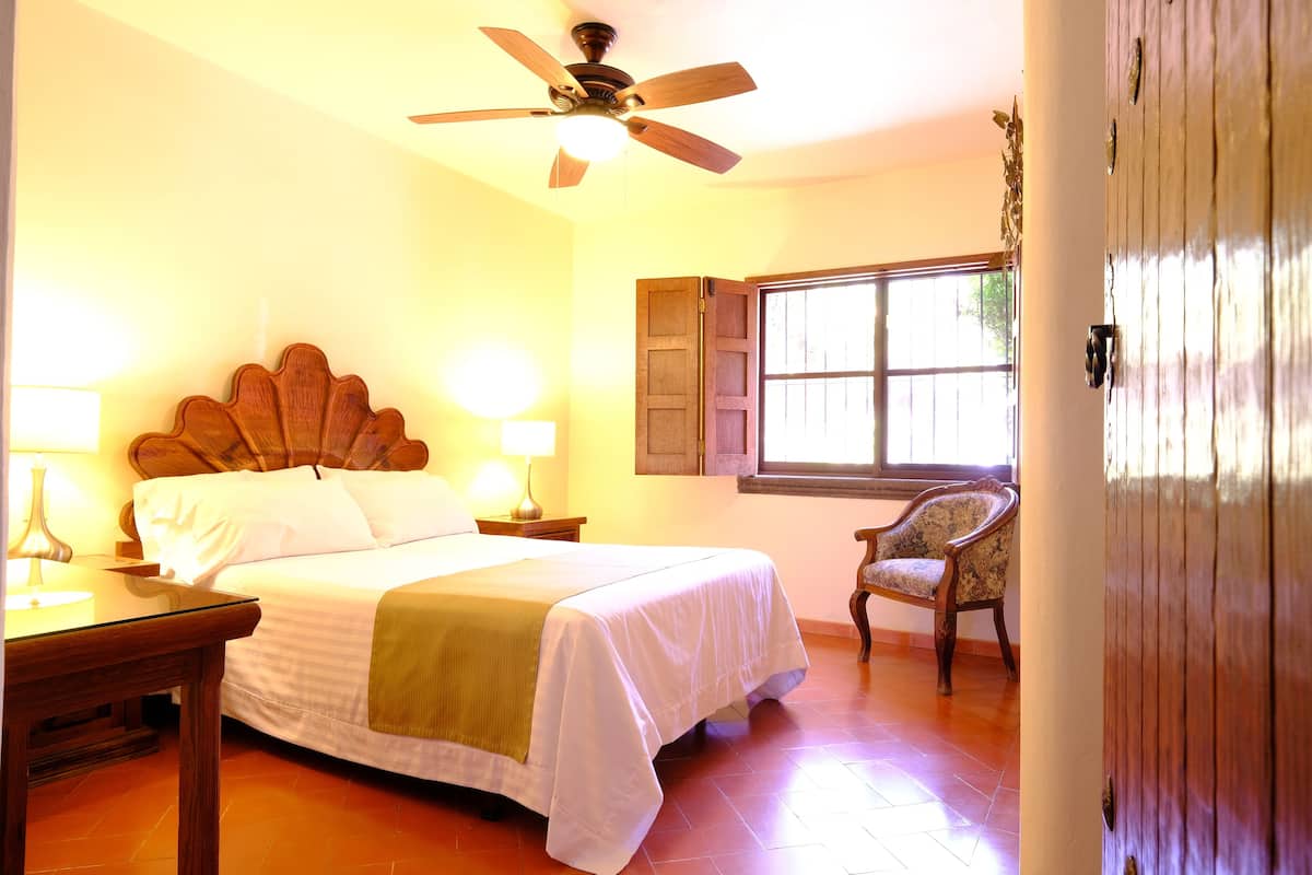 A hotel room with a bed, bedside lamps, a chair, a wooden door, and a window.