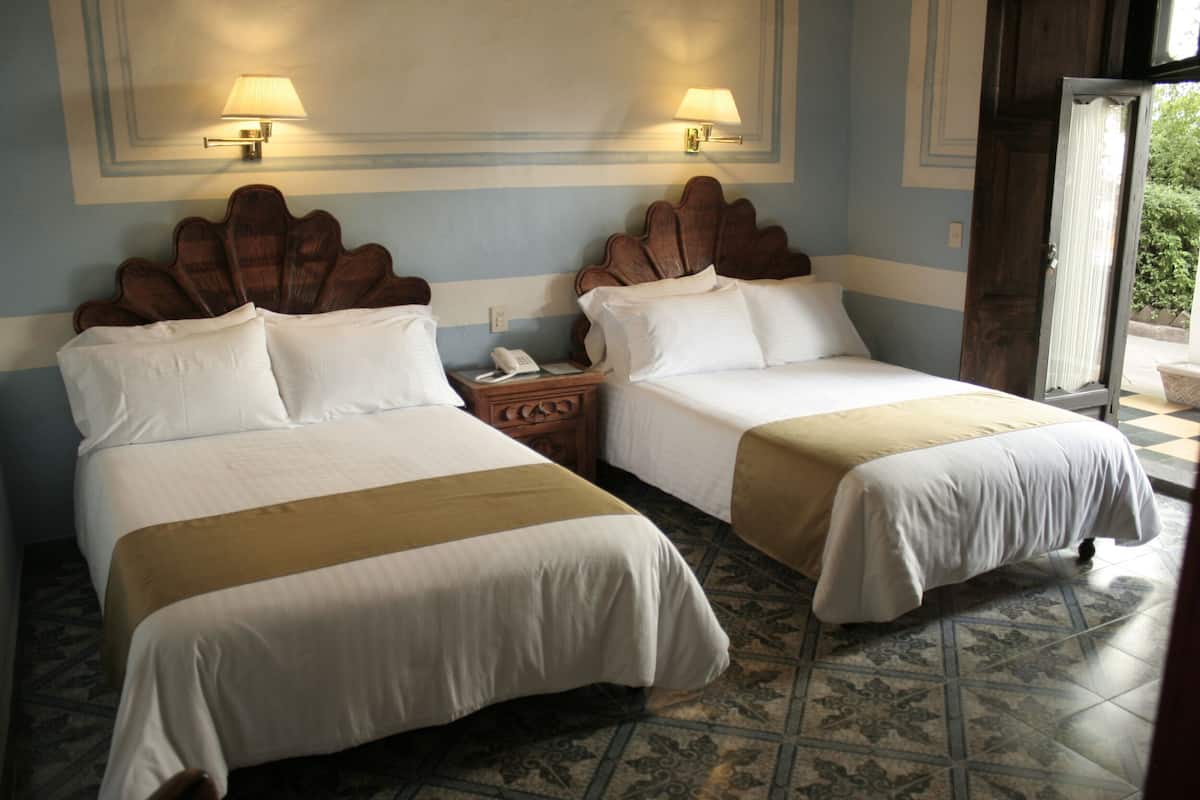 Two single beds with wooden headboards, a nightstand with a telephone, and a patterned tile floor.