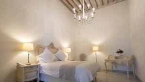 A bedroom with a bed, two bedside tables with lamps, a nightstand, a dresser, and a chandelier.