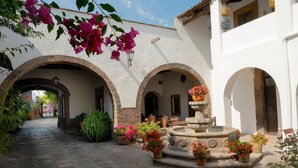 A courtyard with stone flooring, arches, and a central fountain surrounded by potted plants.