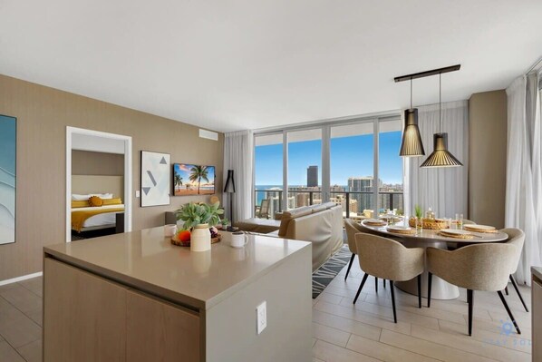 A modern hotel room with a dining area, large windows, and a city view.