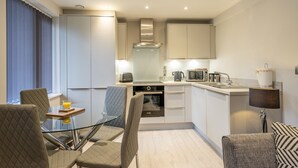 A modern kitchen with a dining area, featuring a glass table, cushioned chairs, and contemporary appliances. - 14 St Johns Mews - sleeps 3 guests  in 1 bedroom (York)