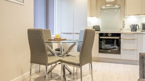 A modern kitchen with a glass dining table, two chairs, a Bosch oven, and a coffee maker. - 14 St Johns Mews - sleeps 3 guests  in 1 bedroom (York)