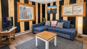 A living room with a sectional sofa, a coffee table, a TV on a wooden stand, and framed pictures on the walls.