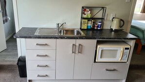 Una kitchenette compacta con un fregadero, un microondas y una repisa con diversos alimentos.