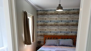 Un dormitorio con cabecera de madera, cama con colcha estampada, lámpara colgante y ventana con cortinas.