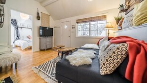 A cozy living room with a sofa, a television, and a dining area with a table and chairs. - Downtown Cabin on Quiet Hilltop. Airy Deck & Views (Estes Park)