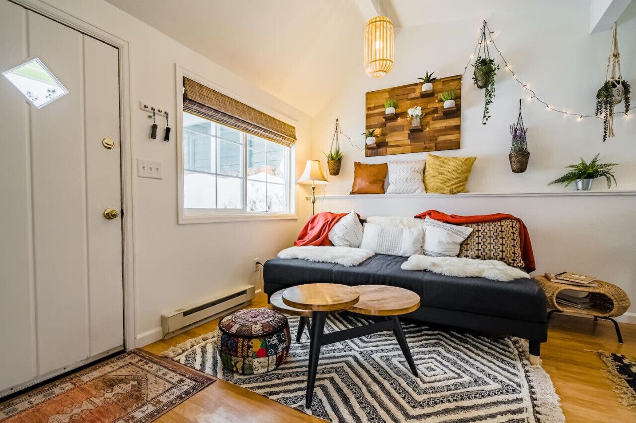 Un salon chaleureux avec un canapé foncé, un tapis à motifs, une petite table en bois et une étagère à plantes fixée au mur.