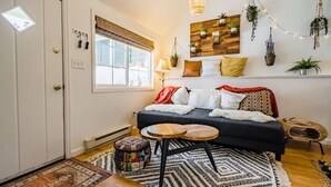 A cozy living room with a dark sofa, a patterned rug, a small wooden table, and a wall-mounted plant shelf. - Downtown Cabin on Quiet Hilltop. Airy Deck & Views (Estes Park)