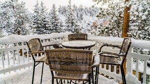A snow-covered outdoor seating area with wicker chairs and a table, surrounded by a white fence and snow-laden trees. - Downtown Cabin on Quiet Hilltop. Airy Deck & Views (Estes Park)