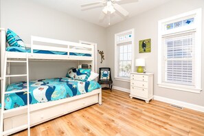 A child's bedroom with bunk beds, a desk, and a window with blinds.