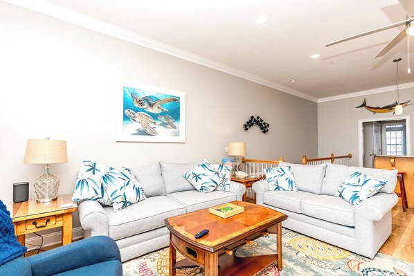 A living room with two sofas, a coffee table, a lamp, a painting, and a ceiling fan.