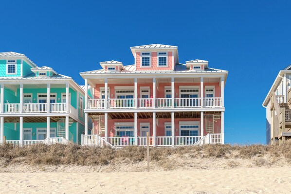 A beachfront property with multiple-story buildings, featuring balconies and a sandy beach in the foreground.
