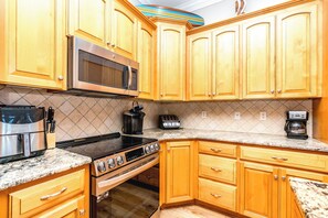 A kitchen with wooden cabinets, a stainless steel microwave, a toaster, a coffee maker, and a stove. - Anchors Away - Stunning 5BR Oceanfront Home - Elevator, Comm. Pool (Surf City)