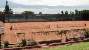 A tennis court with a net, surrounded by a fence and some greenery.