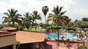 A pool area with a tiled roof, outdoor seating, and palm trees.