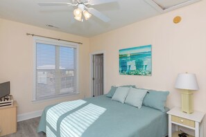Un dormitorio con una cama, ventilador de techo, un cuadro y una lámpara de noche.