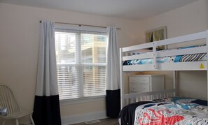 A room with a bunk bed, a desk, a chair, and a window with curtains.