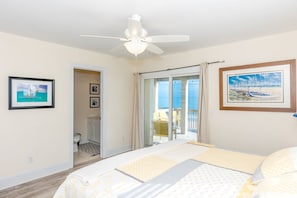A bedroom with a bed, a ceiling fan, a bathroom with a toilet, and a balcony with chairs.