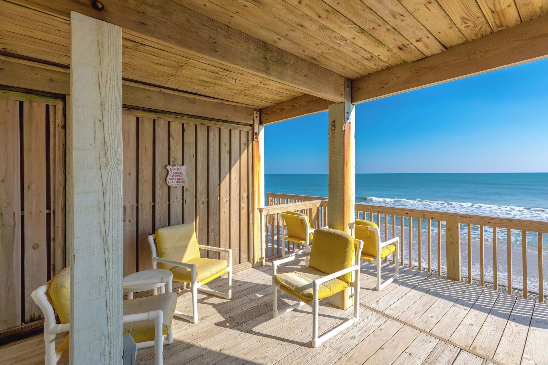 A wooden deck with yellow chairs overlooking the ocean.