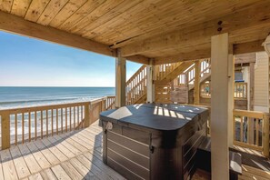 Una terraza de madera con un jacuzzi, barandas de madera y vista al océano.