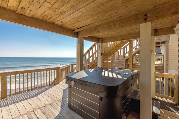 A wooden deck with a hot tub, wooden railings, and a view of the ocean.