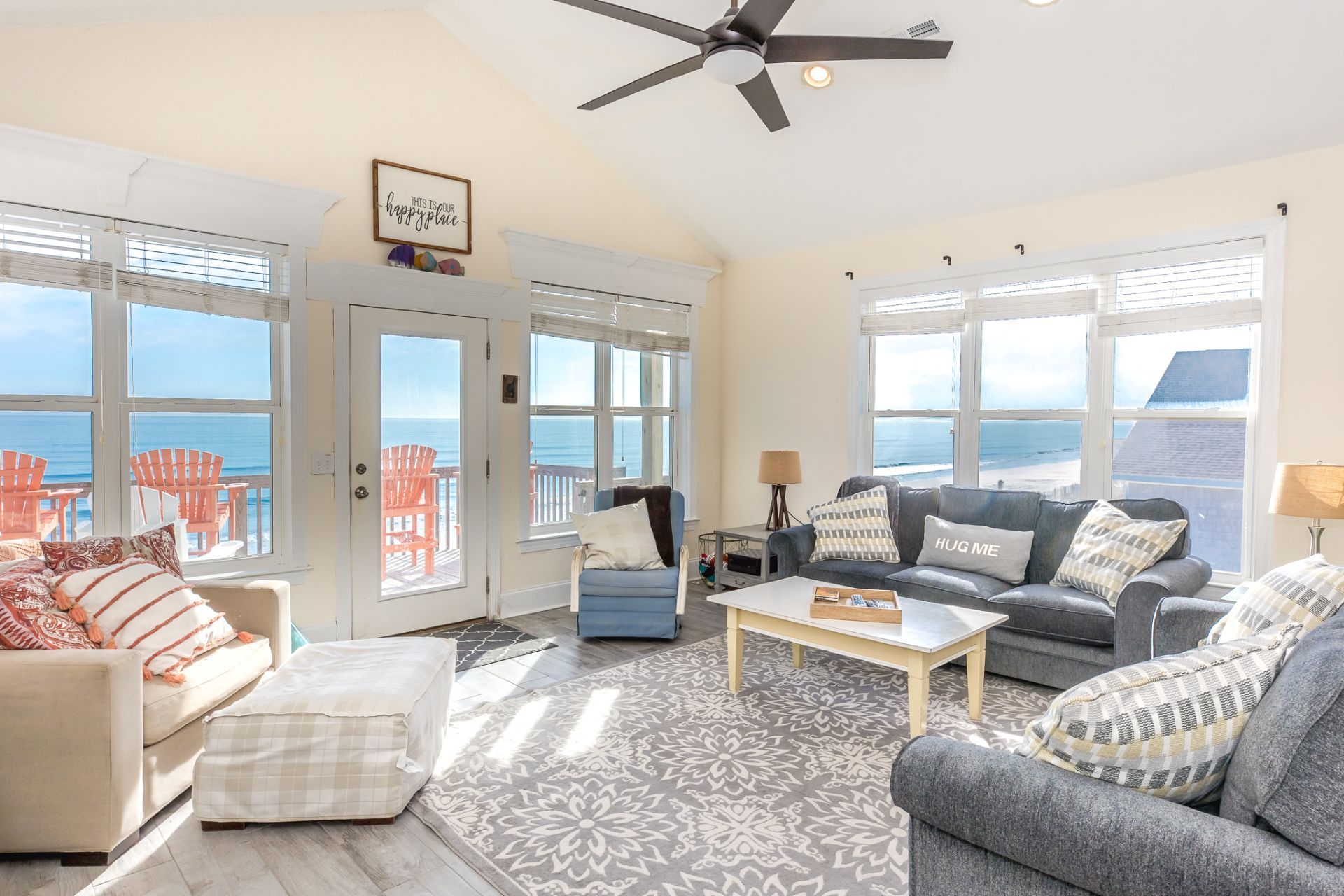A spacious living room with a view of the ocean, a ceiling fan, and a cozy seating area.