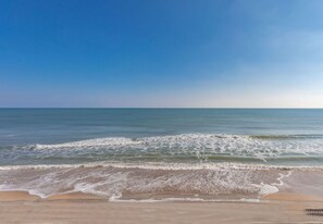 A beach with waves approaching the shore under a clear sky.