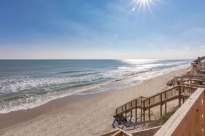 A beach with a wooden walkway leading to a building with a balcony.