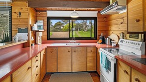 A compact kitchen with wooden cabinets, a built-in oven, and a window offering a view of a garden.